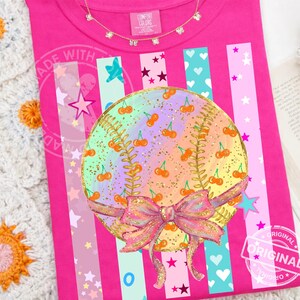 May include: A vibrant pink t-shirt featuring a baseball design. The baseball is adorned with cherries and a bow. The shirt has vertical stripes with stars, hearts, and other shapes. The text "ORIGINAL" is stamped on the shirt.
