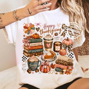 May include: A white t-shirt featuring a graphic print with the text Happy Thanksgiving. The design includes a stack of books, a pumpkin spice latte, a candle, a slice of pie, pumpkins, a leopard print bow, and autumn-themed floral accents.