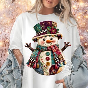 May include: A white t-shirt featuring a colorful snowman graphic. The snowman wears a patchwork top hat with a flower, a matching scarf, and three buttons on its torso. The design includes various patterns like leopard print and floral motifs.