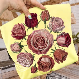 Puede incluir: Una funda de almohada amarilla con un diseño circular de rosas de tela en tonos rojos, rosas y burdeos. Las rosas tienen tallos y hojas verdes. La funda de almohada tiene un diseño cosido y la palabra "ORIGINAL" está estampada en la parte inferior izquierda.