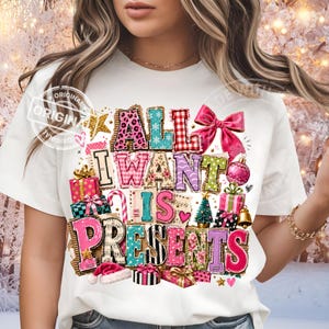 以下が含まれることがあります： 「ALL I WANT IS PRESENTS」という文字が描かれたカラフルなグラフィック付きの白い半袖Tシャツ。ヒョウ柄、チェック柄、花柄などの様々なパターンに加え、ギフトボックス、リボン、ツリーのイラストがデザインされています。