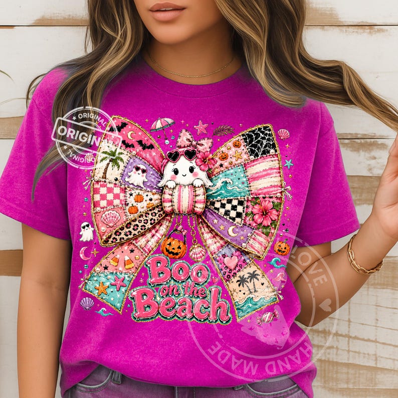 May include: A magenta t-shirt featuring a large, colorful bow design with a ghost wearing sunglasses. The bow includes patchwork patterns, pumpkins, and the text "Boo on the Beach". The shirt has a vintage, slightly faded look.