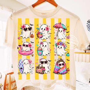 May include: A cream-coloured t-shirt featuring a graphic print of nine white ghosts in various summer-themed activities. The ghosts are arranged over vertical yellow stripes and are decorated with items like sunglasses, flowers, beach gear, and pumpkins.