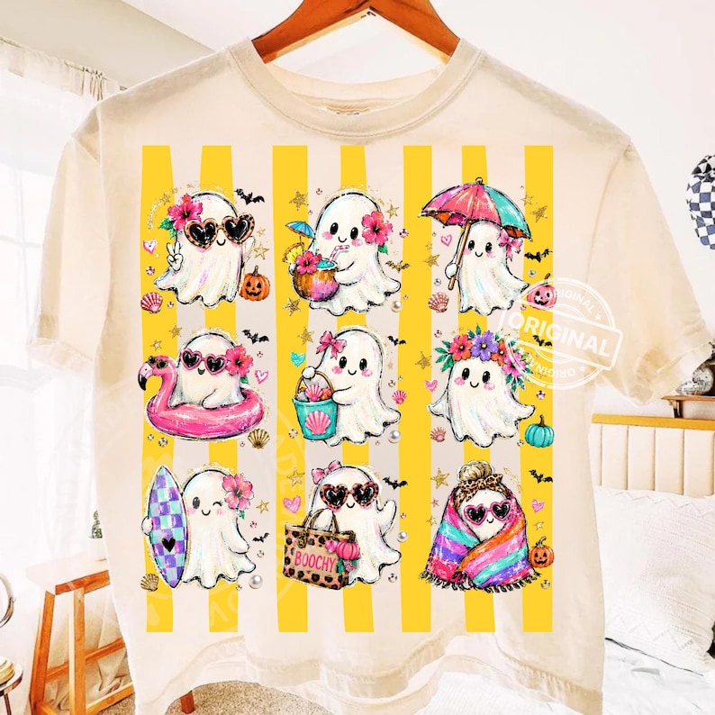 May include: A cream-coloured t-shirt featuring a graphic print of nine white ghosts in various summer-themed activities. The ghosts are arranged over vertical yellow stripes and are decorated with items like sunglasses, flowers, beach gear, and pumpkins.