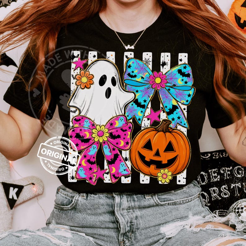 以下が含まれることがあります： ハロウィーンをテーマにしたデザインの黒いTシャツ。グラフィックには、白い幽霊、2つのカラフルなリボン、オレンジ色のジャック・オー・ランタンが含まれています。リボンは、コウモリと月のあるピンクと青の色使いです。デザインはストライプの背景に設定されています。