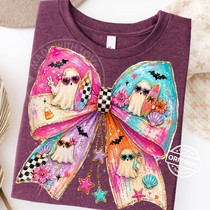 Pu&ograve; includere: Una maglietta viola con un grande fiocco colorato con personaggi fantasma con occhiali da sole. Il fiocco &egrave; decorato con pipistrelli, stelle, fiori e conchiglie. Il testo "MADE WITH LOVE" &egrave; visibile sulla maglietta.