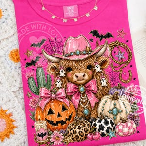 Puede incluir: Camiseta rosa intenso con un dise&ntilde;o caprichoso de Halloween. Una vaca con sombrero y lazo rosa est&aacute; rodeada de calabazas, fantasmas y cactus. La camiseta incluye el texto "MADE WITH LOVE" y "ORIGINAL".