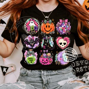 Pode incluir: Uma t-shirt preta com uma grelha de nove gráficos coloridos com o tema de Halloween, incluindo um fantasma com o texto BOO Club, uma abóbora, uma bola de discoteca, um morcego, uma bota, um coração com caveira, uma poção com o rótulo Spooky Vibes, um balde de doces e uma lua.