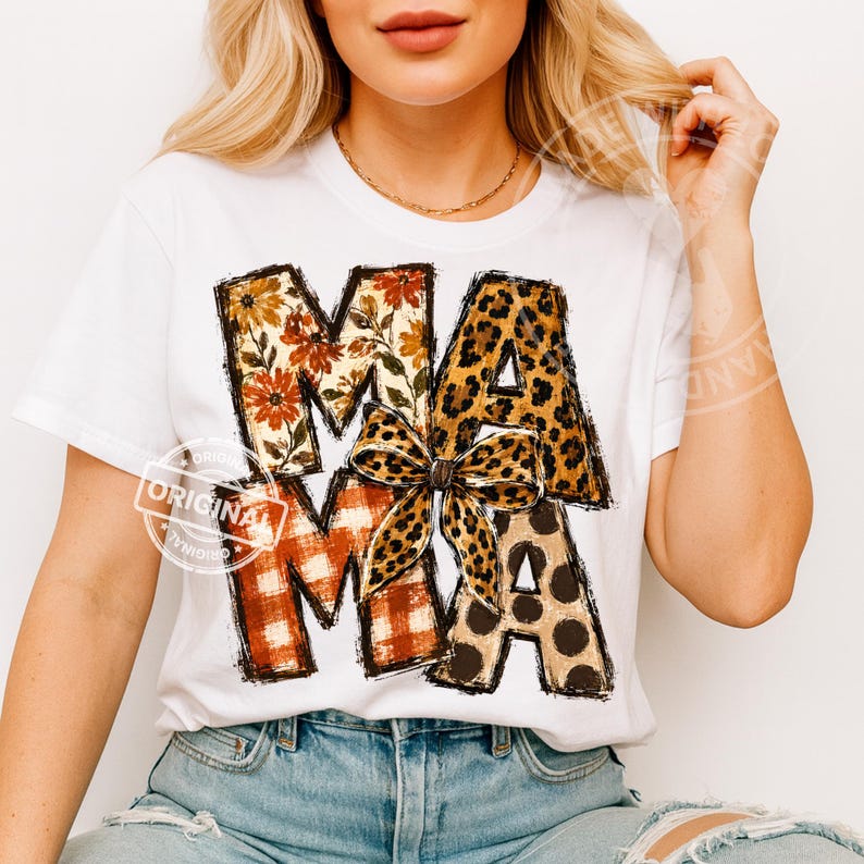Puede incluir: Una camiseta blanca de manga corta con la palabra MAMA en letras grandes. Las letras est&aacute;n rellenas con varios patrones, incluyendo estampados florales naranjas, cuadros rojos y blancos, manchas de leopardo y un lazo central.
