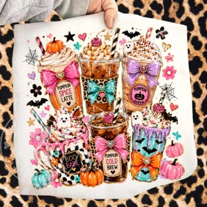 May include: A white Halloween-themed design featuring six decorative beverages, including pumpkin spice lattes and cold brews, adorned with bows, pumpkins, and spooky accents. The design includes text such as "Pumpkin Spice Latte" and "Boo Babe".