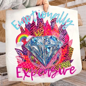 Może przedstawiać: Biała torba typu tote z napisem "Emotionally Expensive" w żywym, kolorowym wzorze. Projekt przedstawia duży, błyszczący niebieski diament otoczony tęczą, płomieniami i zwierzęcymi wzorami.