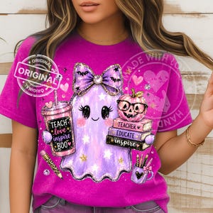 May include: A bright magenta t-shirt featuring a graphic of a light purple ghost wearing a glittery bow, holding a tumbler with the text TEACH love inspire BOO, sitting next to a stack of books labeled TEACHER EDUCATE inspire and a pumpkin.