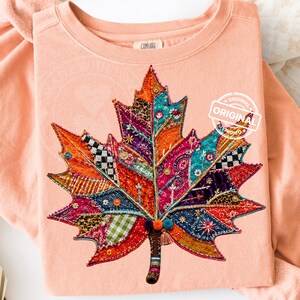 May include: A peach-colored sweatshirt featuring a large, central maple leaf graphic composed of various colorful fabric patches, intricate embroidery, sequins, and small pom-poms. The interior neck label reads COMFORT and a circular watermark says ORIGINAL.