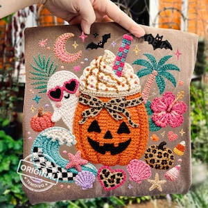 Könnte beinhalten: Ein braunes Stoffquadrat mit einem Häkeldesign, das Halloween- und tropische Elemente kombiniert. Ein orangefarbener Kürbis mit einem Jack-o'-Lantern-Gesicht ist mit einem Getränk mit Schlagsahne belegt. Weitere Elemente sind ein Geist, Fledermäuse und eine Hibiskusblüte.