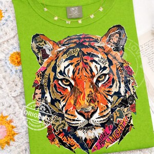 May include: A lime green t-shirt featuring a collage-style tiger face. The tiger's face is composed of various images and text fragments, including the words "RESIST", "SHERO", "WILD HEART", and "GIRL POWER". A gold necklace with small flower pendants is visible.