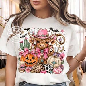 Puede incluir: Camiseta blanca con un dise&ntilde;o de Halloween. Presenta una vaca de las Tierras Altas con un sombrero de vaquero rosa, calabazas, fantasmas y flores. La palabra "ORIGINAL" est&aacute; estampada en la camiseta.