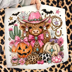Puede incluir: Un coj&iacute;n cuadrado blanco con una vaca de las Tierras Altas que lleva un sombrero de vaquero rosa, rodeada de calabazas de Halloween, murci&eacute;lagos y fantasmas. La vaca tiene un gran lazo rosa y est&aacute; adornada con joyas turquesas. El dise&ntilde;o incluye un cactus, estrellas y una herradura.