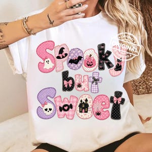 May include: A white t-shirt featuring the text Spooky but Sweet in large, colorful, patterned letters. The letters are decorated with Halloween-themed icons including a ghost, witch hat, bat, pumpkin, spider, skull, and haunted house in pink, purple, and black.
