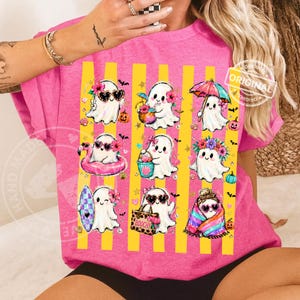 May include: A bright pink t-shirt featuring a graphic print of nine white ghosts in various summer activities, including surfing, swimming with a flamingo float, and holding a beach bag labelled BOOCHY, set against vertical yellow stripes.