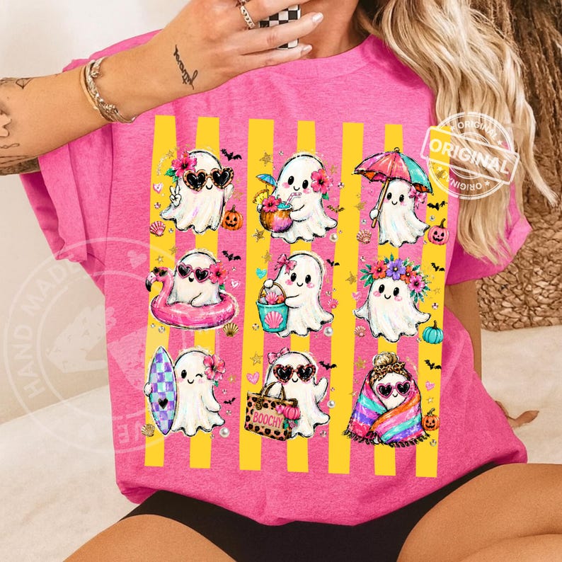 May include: A bright pink t-shirt featuring a graphic print of nine white ghosts in various summer activities, including surfing, swimming with a flamingo float, and holding a beach bag labelled BOOCHY, set against vertical yellow stripes.
