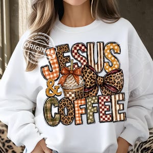May include: A white long-sleeve sweatshirt featuring a graphic print with the text JESUS & COFFEE. The design includes a central iced coffee cup with a bow, surrounded by letters patterned with leopard print, red plaid, and polka dots.