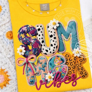 Pode incluir: Camiseta amarela com as palavras "SUMMER VIBES" em um design colorido e texturizado. As letras são adornadas com detalhes florais e de estampa animal. A camiseta tem uma pequena etiqueta que diz "Comfort Colors".