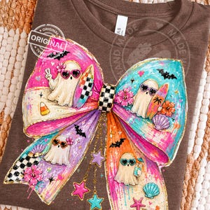Pu&ograve; includere: T-shirt marrone con un grande disegno a fiocco colorato con personaggi fantasma che indossano occhiali da sole e tavole da surf. Il fiocco ha un centro a scacchi ed &egrave; decorato con pipistrelli, stelle e conchiglie. La maglietta ha le parole "Original" e "Hand Made".