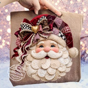 Op de afbeelding: Een decoratief kerstman-gezicht met een donkerrode fluwelen muts, een gouden hartvormige bedel, een zwart-wit geblokte strik en een gelaagde stoffen baard. De kerstman heeft blauwe ogen, roze wangen en een gedetailleerde witte snor en baard.