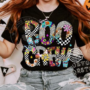 May include: Black t-shirt with the words "BOO CREW" in a colorful, patterned design. The letters feature Halloween-themed patterns, including pumpkins, ghosts, and checkered patterns. The shirt has a round neckline and short sleeves.