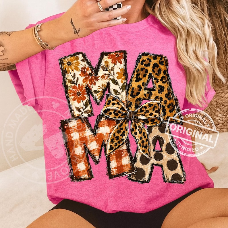 Puede incluir: Una camiseta rosa brillante con la palabra MAMA en letras grandes. Cada letra tiene un patr&oacute;n diferente: floral, estampado de leopardo y cuadros naranjas. Un lazo con estampado de leopardo est&aacute; centrado sobre las letras. Manga corta.