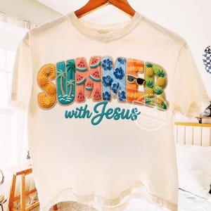 May include: Cream-colored t-shirt with the word "SUMMER" in colorful, textured letters, each designed with summer-themed elements like sunflowers, palm trees, and watermelons. The phrase "with Jesus" is embroidered below. A pair of sunglasses is included in the word "SUMMER".