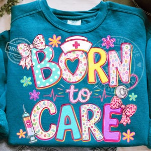 K&ouml;nnte beinhalten: T&uuml;rkisfarbenes Sweatshirt mit dem Schriftzug "BORN to CARE" in bunten, floral gemusterten Buchstaben. Das Design umfasst eine Krankenschwesterm&uuml;tze, ein Stethoskop, eine Spritze und Schleifen. Das Sweatshirt hat einen Rundhalsausschnitt.