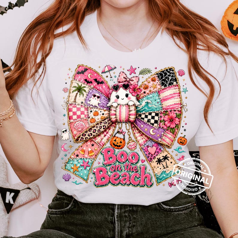 May include: White t-shirt featuring a colorful bow design with a ghost character wearing sunglasses. The bow is made of patchwork patterns with beach and Halloween elements. Text reads "Boo on the Beach".