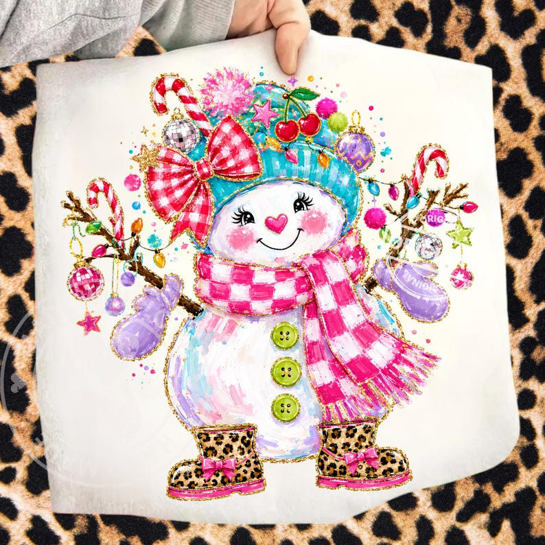 May include: A white snowman graphic print featuring a teal hat, a pink and white checkered scarf, and three green buttons. The snowman wears leopard print boots with pink bows and holds candy canes and ornaments on brown branch arms.