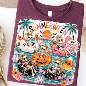 May include: A maroon t-shirt featuring a colorful graphic with the text "SUMMERWEEN". The graphic depicts skeletons in swim rings, palm trees, bats, and a sunset. The skeletons are wearing sunglasses and holding drinks.