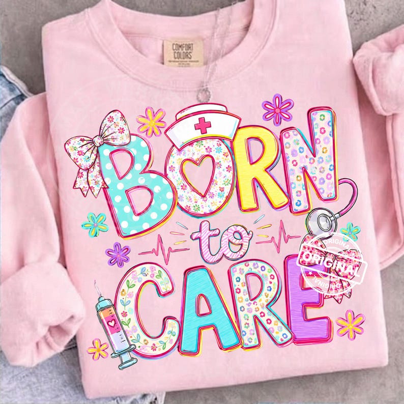 K&ouml;nnte beinhalten: Hellrosa Sweatshirt mit dem Schriftzug "BORN to CARE" in bunten, gemusterten Buchstaben. Das Design umfasst einen Krankenschwesterhut, ein Stethoskop, eine Spritze und florale Akzente. Eine Schleife und Blumen verzieren die Buchstaben.