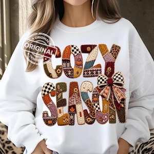 Peut inclure: Un sweat-shirt blanc à manches longues avec l'inscription COZY SEASON en grandes lettres. Chaque lettre est remplie d'un patchwork de motifs automnaux, incluant des citrouilles, des feuilles, des tournesols, du tartan et des imprimés léopard.