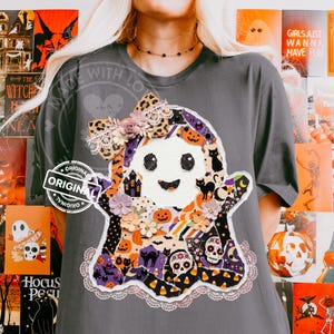 May include: A charcoal gray t-shirt featuring a large ghost-shaped graphic made of various patterned fabric patches. The ghost is decorated with a leopard print bow, small fabric flowers, and lace trim, displaying motifs of pumpkins, cats, and skulls.