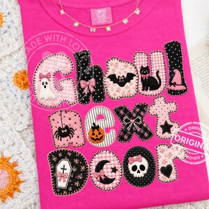 May include: A bright pink t-shirt featuring the text GHOUL NEXT DOOR in large, fabric-appliqued letters. Each letter is decorated with patterns like gingham, polka dots, and florals, and includes icons like a ghost, bat, cat, spider, and skull.