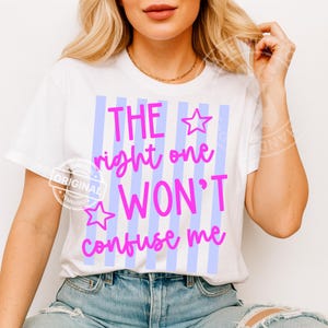 May include: White t-shirt with the text "THE right one WON'T confuse me" in pink script. The text is set against a background of vertical light blue stripes. The shirt has a round neckline and short sleeves.
