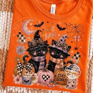 May include: Orange t-shirt with a Halloween-themed graphic. Two black cats wearing witch hats and scarves are featured, along with pumpkins, bats, and the text "Boo Babe" and "Stay Spooky".