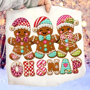 May include: A white fabric panel featuring three embroidered gingerbread people wearing patterned hats and bow ties, decorated with colorful buttons and snowflake accents. Below the figures, the text OH SNAP is embroidered in large, multi-colored patterned letters.