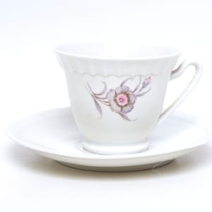 Peut inclure: Service à thé blanc composé d'une tasse et d'une soucoupe. La tasse présente un motif floral avec des accents roses et gris. La tasse a une anse incurvée et un bord festonné. La soucoupe est ronde et unie.