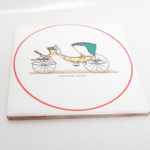 May include: Square ceramic tile featuring a vintage illustration of a yellow and green horse-drawn carriage within a red circular border. The text "PICCOLOMINI CALECHE" is below the carriage image. The tile has a white background.