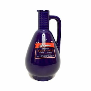 May include: A vintage, deep blue ceramic decanter with a handle and a spout. The decanter has a label that reads "Arrow De Luxe Rock & Rye". The bottle is 4 quarts.