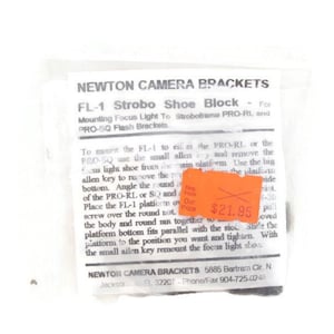 May include: A clear plastic bag containing a Newton Camera Brackets FL-1 Strobo Shoe Block. The packaging includes text detailing mounting instructions for focus lights and flash brackets. An orange price tag is visible.