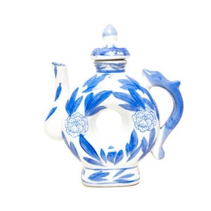 May include: White and blue ceramic teapot with a unique circular design. The teapot features blue floral patterns and a dolphin-shaped handle. The lid is topped with a small finial. A decorative piece for the kitchen.