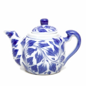 May include: A small, white ceramic teapot with a blue floral design. The teapot has a curved handle, a spout, and a lid with a small knob. The blue pattern features leaf-like shapes. A decorative item for tea lovers.
