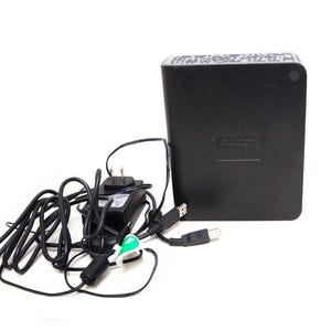 Op de afbeelding: Een zwarte externe harde schijf met een voedingsadapter en USB-kabel. De harde schijf heeft het "WD"-logo. De voedingsadapter en kabel zijn zwart.