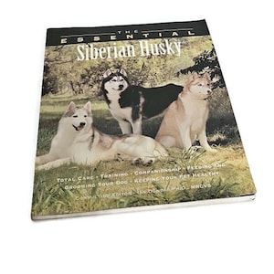 Puede incluir: Un libro titulado "The Essential Siberian Husky" con tres Huskies siberianos en la portada. Los perros están en un entorno exterior cubierto de hierba. La portada del libro incluye texto sobre el cuidado de los perros.
